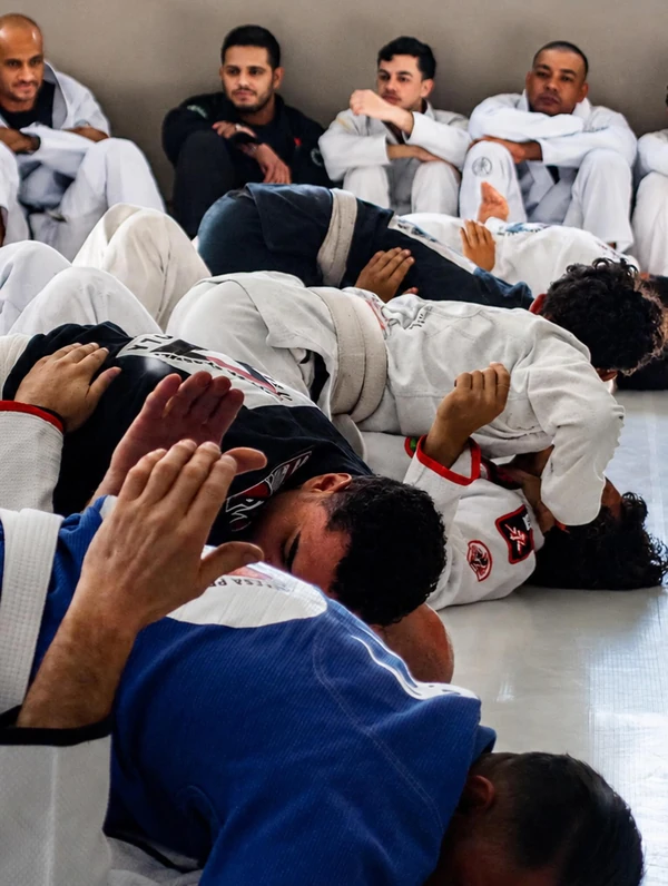 Alunos praticando técnicas em duplas, com colegas acompanhando ao fundo
