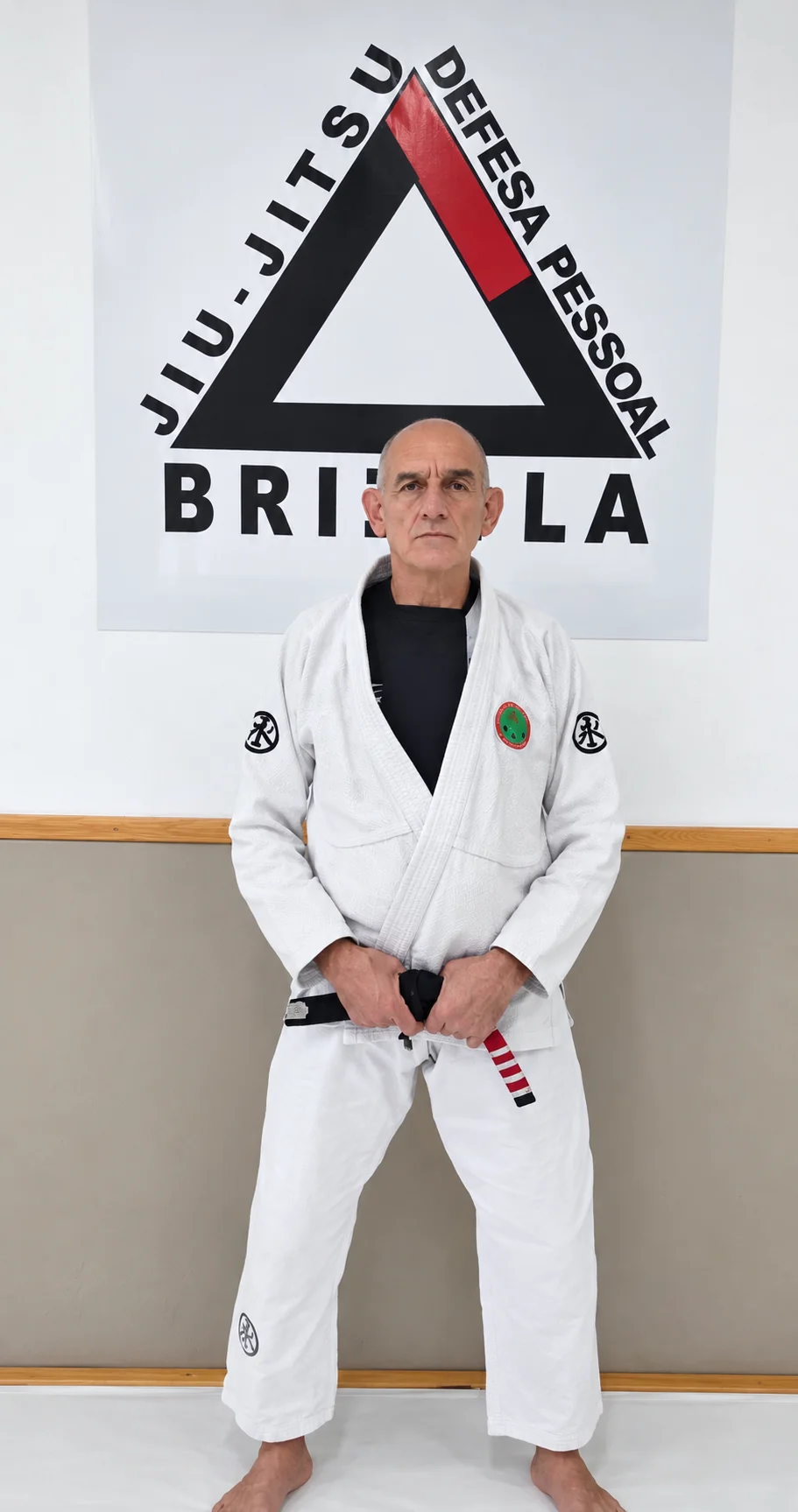Professor Brizola, de quimono branco e faixa preta, diante da marca da academia
